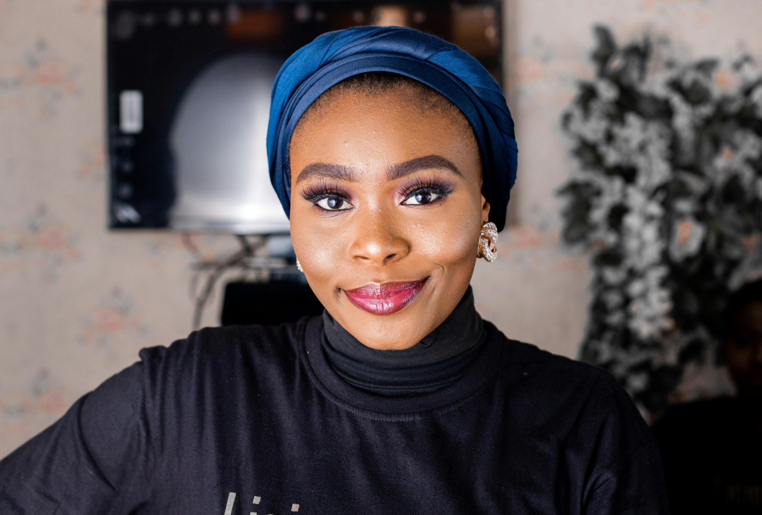 Vibrant portrait of a smiling woman indoors wearing a blue turban and stylish black turtleneck.